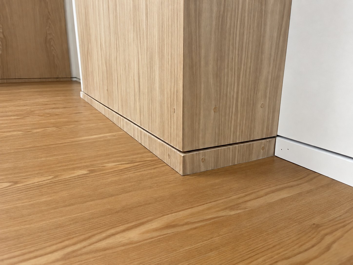 Visible wood plugs above a continuous base reveal at an oak paneled corner